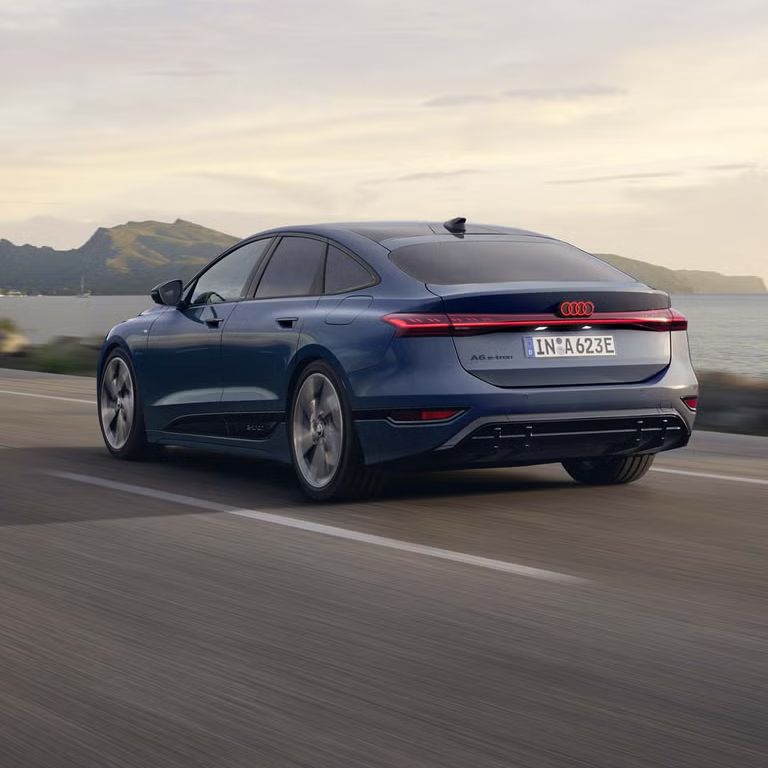 A6 Sportback e-tron, z pohľadu na zadnú časť, jazdí po ceste popri pobreží. V pozadí sú vidieť hory. 