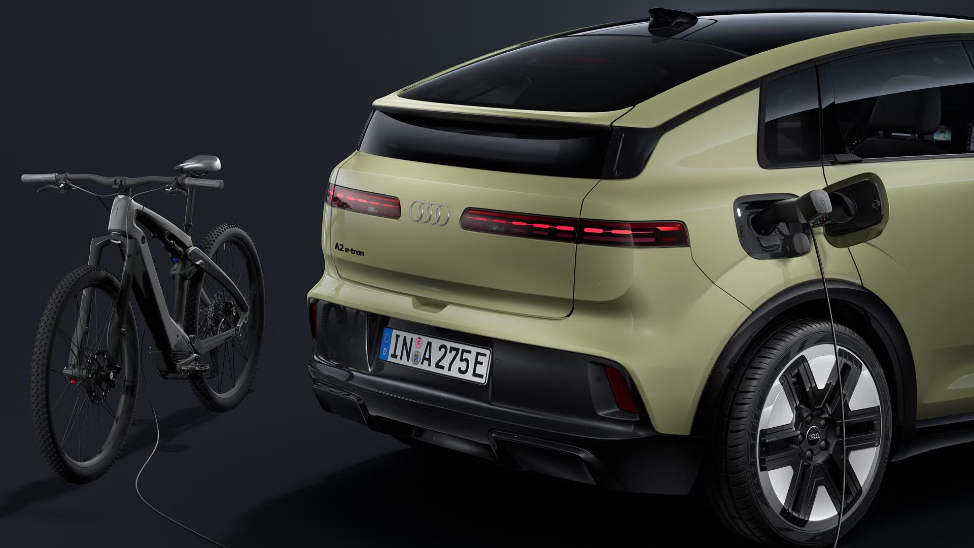 Detailný záber na zadné partie. Napájací kábel je pripojený k otvorenému nabíjaciemu portu Audi A2 e-tron, ktorý nabíja elektrobicykel za vozidlom.